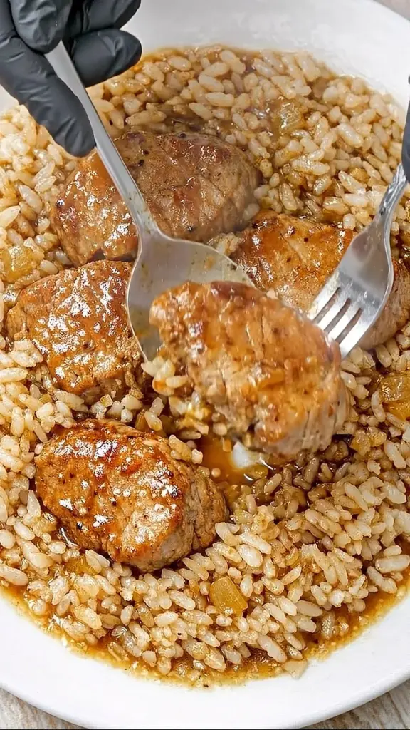 Tender garlic butter beef medallions with onion rice dish served on a plate.